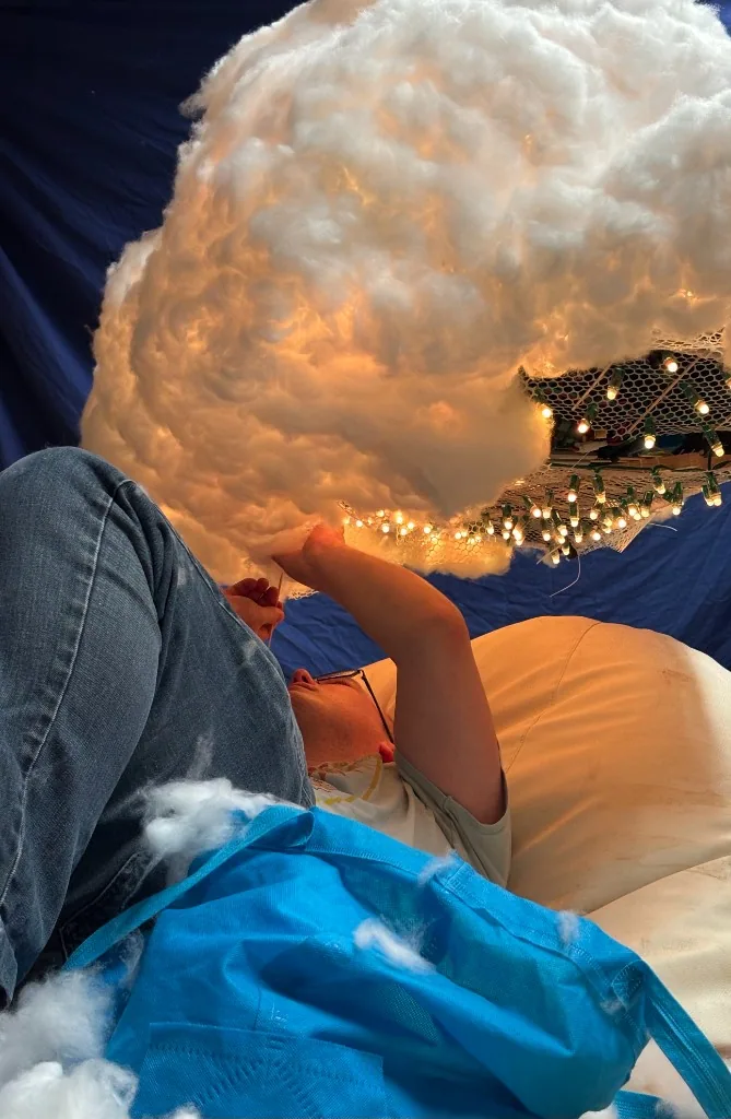 A person filling a large illuminated handmade cloud with fibre