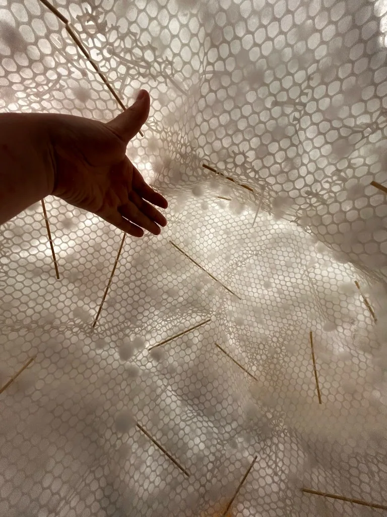 A hand testing the translucent mesh and fibre structure inside the cloud